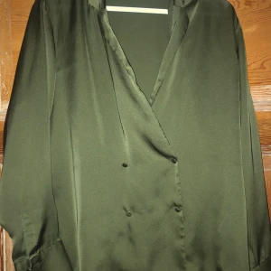 Mörkgrön sidenblus  - Superfin mörkgrön sidenblus med guldknappar! Fina ärmar och en fin passform. Prefekt till ett par svarta jeans till vardags eller skinnbyxor till fest! Köparen står för frakten och det angivna fraktpriset kan ändras! 