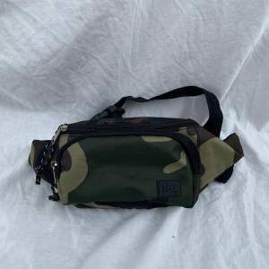 En snygg midjeväska/magväska i grön kamouflage från lager 157. Väskan är rymlig och passar väldigt bra till svart.