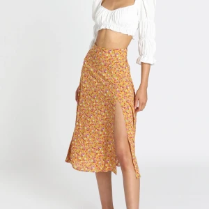 Gul blommig kjol med slits (storlek 36) - Superfin blommig orange/gul kjol från Showpo, storlek 36 (AU 8). Helt ny och oanvänd. Jag köpte kjolen för 370kr (plus tullavgift, totalt 520kr). Köpare står för frakten.