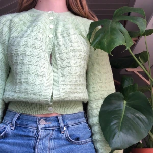 En ljusgrön kofta - En ljusgrön stickad kofta med med vita, snäckskimmrande knappar. Plagget är köpt på second hand och har sparsamts användts av mig. Storleken är Xs. 