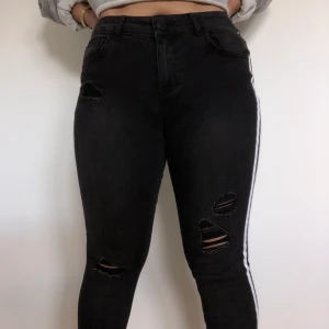 Svarta jeans lätt ripped med vit detalj - HELT NYA OANVÄNDA! Säljer superstretchiga, högmidjade och jättesköna jeans med lite rip och vita band på kanten. Säljer då jag fick de som present och de inte är min stil. Jättefin passform som framhäver former och underbart skönt material. Frakt ingår ej
