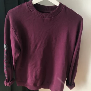 Sweater - Vinröd/lila tröja från nakd som är supermysig med gråa rosor inbroderade på underarmarna. Lite oversized. Frakten blir 44kr🌻