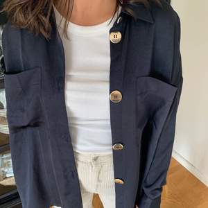 En helt oanvänd skjorta från Gina Tricot, lappen sitter kvar! Köpt för 349kr. Skjortan är marinblå i silkes liknande tyg, med guldknappar som detalj & i oversize modell 💙. Frakt ingår ej. 