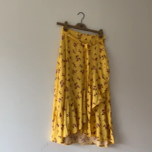 Gulblommig kjol  - Gul kjol med röda blommor på. Jätte fin och oanvänd från Kappahl. Den har volanger som går omlåt. 