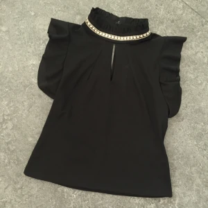  - Svart kortärmat tröja/topp med en smycke rund halsen. Rent och hel. Knappt använd. Stl 42. Passar till M/L-L.