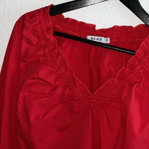 34, red blouse - The model should sit loosely on.  It has a v-neck and is long-sleeved.  It goes a little under the belly, but besides that it has a regular fit.  It is an expired model