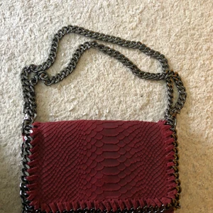 Väska  - Vinröd väska med alligator imitation. Mocka material. Den har långa band egentligen men man kan fixa så de blir kortare som på bilden!