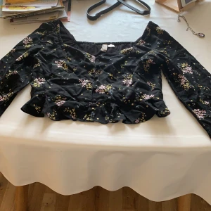 Blommig tröja  - En tröja i kort modell   Storlek 42   Svart med blommor på