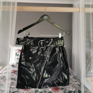 Kjol  - En kort kjol från H&M i svart tyg med lackad effekt [frakt tillkommer] 