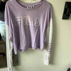 Lila fila tröja storlek large  - Lila fila tröja storlek large. Den är ganska kort i modellen. Inte riktigt en magtröja men ändå lite kortare, kan skicka fler bilder om du vill. Den har en liten liten missfärgning på framsidan, kan skicka fler bilder vid intresse som sagt. 