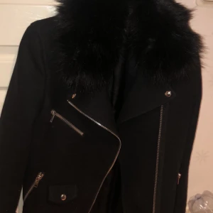 Svart kappa från Zara med pälskrage - En svart kappa från Zara med pälskrage och silvriga detaljer. Köpt för cirka 2 år sedan knappt använd.