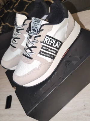 Vita och beige sneakers från Replay - Snygga sneakers från Replay i vitt och beige med svarta detaljer och text på sidan. Skorna har meshpartier för extra andningsförmåga, svarta skosnören och en vit sula. Märket Replay syns tydligt på sidan och tungan. Perfekta för en trendig streetstyle. Helt nya storlek 42 