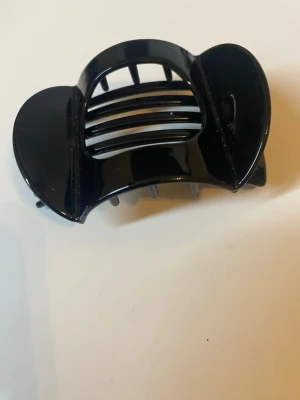  Svart hårklämma i plast - Stilren svart hårklämma med breda grepp och rundad form. Perfekt för att snabbt sätta upp håret och hålla det på plats. Tillverkad i blank plast med klassisk design som passar till många olika frisyrer.