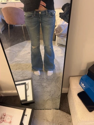 Blå bootcut jeans med slitningar - Säljer ett par ljusblå bootcut jeans med slitningar och hål på båda benen och röda tråd detaljer. Max använda 2 gånger och säljs för att dom inte används längre. Det är ett litet hål vid gylfen vilket jag inte tycker syns så mycket men även därför jag säljer ganska billigt.