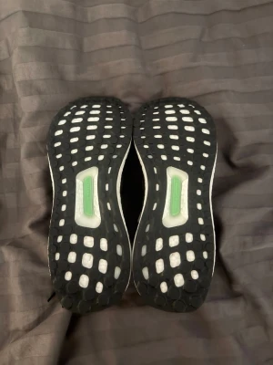 Svarta sneakers med vit sula - Snygga svarta sneakers med vit sula och svart ovandel i mesh. Skorna har svarta skosnören och detaljer i grönt på undersidan. Perfekta för en sportig och modern look.