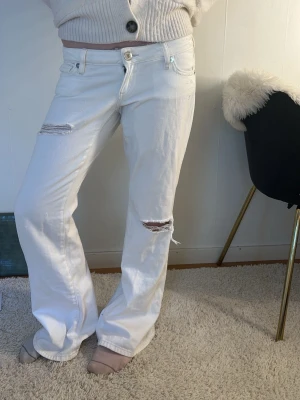 Vita raka jeans med slitningar - Säljer ett par vita jeans med raka ben och slitna detaljer vid knä och lår. Jeansen har klassisk femficksmodell och låg midja. Perfekta för en avslappnad och trendig look.