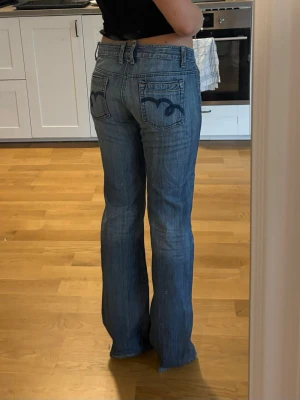 Blå bootcut jeans med broderade fickor - Säljer ett par blå lågmidjade bootcut jeans med snygga broderade detaljer på bakfickorna. 