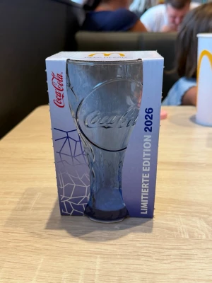 Coca-Cola glas Limited Edition 2026 - Säljer ett exklusivt Coca-Cola glas från McDonald's, Limited Edition 2026. Glaset är genomskinligt med en lätt blå ton och har Coca-Cola-loggan ingraverad. Levereras i originalförpackning med snygg design och samlarvärde.