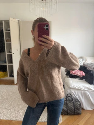 Beige oversized stickad tröja - Mysig beige stickad tröja med v-ringning och avslappnad passform. Perfekt att bära off-shoulder. Använd fåtals gånger och köpt för 500 