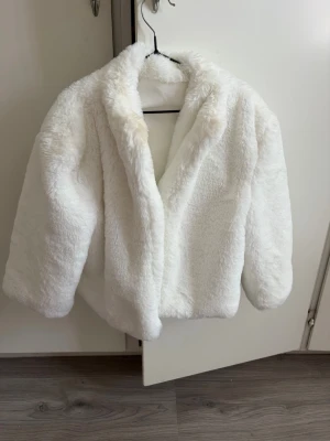 Vit fluffig fuskpälsjacka - Säljer en vit, supermjuk och fluffig fuskpälsjacka med bred krage och rak passform. Jackan har en stilren look och är perfekt för kalla dagar när du vill känna dig extra cozy och trendig.