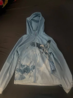 Ljusblå Trapstar jacka - Snygg ljusblå Trapstar windbreaker. Jackan har ett stort tryck av örnar i flykt både fram och bak, samt texten 'TRAPSTAR' på ryggen. Säljs för att den ej passar längre