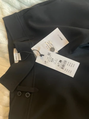 Svarta kostymbyxor från Gina Tricot - Säljer ett par svarta kostymbyxor från Gina Tricot i storlek XXS. Byxorna har raka ben, låg midja och snygga knappdetaljer vid linningen. Materialet är mjukt och har en lätt stretch för extra komfort. Säljer dem pga dem är för korta dem är helt nya med pris lapp endast testade💕💕