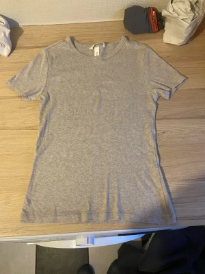 Ljusgrå ribbad t-shirt - En enkel och stilren ljusgrå t-shirt med ribbad struktur. T-shirten har rund halsringning och korta ärmar. Perfekt basplagg som passar till det mesta och är skön att bära tack vare det mjuka materialet.