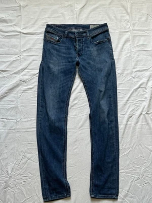 Mörkblå raka jeans med slitningar - Snygga mörkblå jeans med raka ben och diskreta slitningar. Klassisk femficksmodell med knappgylf och kontrastsömmar. Jeansen har en avslappnad passform och passar perfekt till en casual stil.
