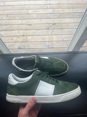 Gröna valentino flacrew  - Snygga sneakers i grön mocka med vita detaljer och vit sula från Valentino. Skorna har klassisk låg profil, gröna skosnören och en vit panel på sidan. Perfekta för dig som vill ha en stilren men ändå unik look.