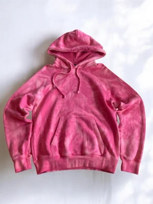 Rosa hoodie från Acne Studios - Säljer en snygg rosa hoodie från Acne Studios med tie-dye effekt. Hoodien har huva med dragsko och en stor magficka framtill. Tillverkad i mjuk bomullsblandning som är skön att ha på sig. Perfekt för dig som gillar streetwear och vill sticka ut.