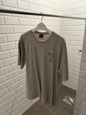 Grå Ralph Lauren t shirt med ficka och logga - Snygg grå Polo Ralph Lauren t-shirt i bomull med rund hals, korta ärmar och en bröstficka med en liten mörkblå broderad logga. Enkel och stilren design som passar till det mesta. Perfekt basplagg för garderoben.