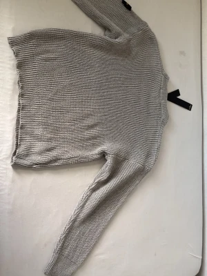 Helt ny ljusgrå stickad tröja Stone Island - Snygg ljusgrå stickad tröja från Stone Island. Tröjan har en klassisk rak passform, rund halsringning och ribbstickade muddar vid ärmslut och nederkant. Perfekt för lager på lager och enkel att matcha med olika outfits.