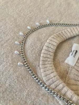 Silverfärgat halsband med pärldroppar - Snyggt halsband i silverfärgad rostfritt med kedja och små vita droppformade pärlor längs hela kedjan. Perfekt för att ge en cool touch till din outfit och passar till många olika stilar. Enkel att matcha med både stickade tröjor och t-shirts.
