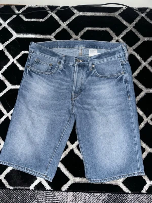 jeansshorts - Säljer ett par blå jeansshorts i klassisk femficksmodell. Shortsen har normal passform, midwaist och är tillverkade i bomull. Perfekta för sommaren och har en tidlös look som passar till det mesta. Jätte bra pris för jeansshorts