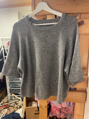 Grå stickad tröja med trekvartsärm - Mysig grå stickad tröja med avslappnad passform och trekvartsärmar. Tröjan har rund halsringning och ribbade kanter. Perfekt för lager på lager och enkel att matcha med olika outfits.