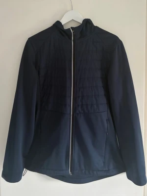 Mörkblå cardigan  - Snygg mörkblå cardigan med hel dragkedja framtill och quiltade detaljer på bröstet. Jackan har huva, två sidofickor med dragkedja och en något längre bakdel. Perfekt för blåsiga dagar och enkel att matcha med olika outfits.