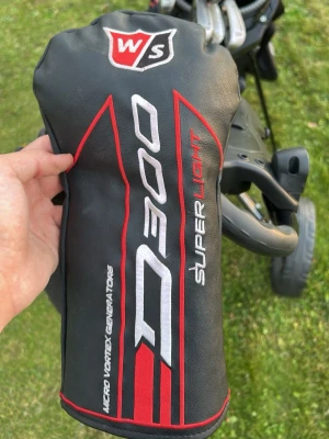 Wilson Staff D300 headcover - Säljer ett svart headcover till golfklubba från Wilson Staff, modell D300 Superlight. Skyddet har röda och vita detaljer samt texten 'Micro Vortex Generators'. Perfekt för att skydda din driver eller träklubba på golfbanan.
