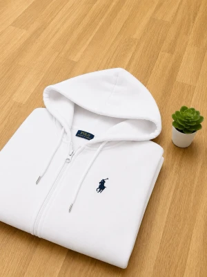 Vit Ralph lauren hoodie - Snygg vit hoodie med dragkedja från Polo Ralph Lauren. Klassisk design med huva, dragsnören och två fickor framtill. Ikoniska mörkblå loggan broderad på bröstet. Tillverkad i mjukt material som känns skönt mot huden.