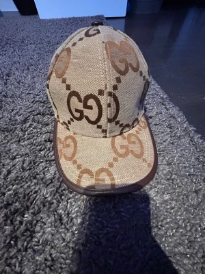 Beige keps med GG-mönster - Säljer en beige keps med brunt GG-mönster och mörkbruna detaljer runt skärmen. Kepsen har en klassisk form och är tillverkad i ett slitstarkt tygmaterial. Perfekt för dig som gillar stilrena accessoarer med tydlig logga.