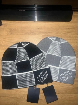 mössor i svart och grått - Två stickade mössor med patchworkmönster i svart, vitt och grått. Ena mössan är svartvit och den andra är gråvit., rundad form. Perfekt för dig som vill ha en unik och trendig accessoar till vintern. Aldrig använd pris kan diskuteras 