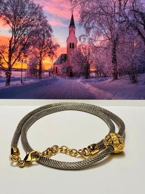 Snyggt halsband/ armband i silver och guld - Stilrent halsband/  armband i silvrig metall med en dekorativ guldfärgad pärla och matchande guldfärgade detaljer. Kedjan är tunn och flätad, vilket ger en modern och elegant känsla. Perfekt accessoar för att lyfta din outfit.