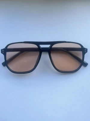 Svarta solglasögon med beige glas - Snygga solglasögon med svart båge och fyrkantig form. Glasen är beige-tonade och ger en cool retrovibe. Perfekta för att lyfta din stil under soliga dagar.