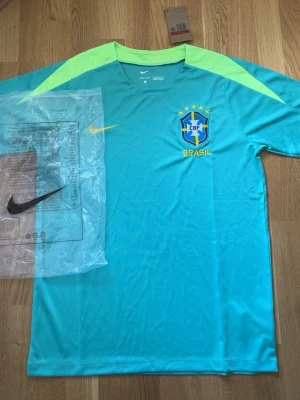 Nike Brasil fotbollströja turkos - Snygg turkos fotbollströja från Nike med Brasil-logga och gula detaljer. Tröjan har korta ärmar, rund hals och är tillverkad i ett lätt, snabbtorkande material som passar perfekt till träning eller match.