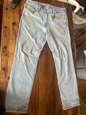 Ljusblå raka jeans - Säljer ett par ljusblå jeans med rak passform från h&m. Jeansen har normal midja, bälteshällor och är tillverkade i ett mjukt denimtyg. Perfekta för en avslappnad och trendig look. Det är ett litet hål på knät men annars så är det bra skick.