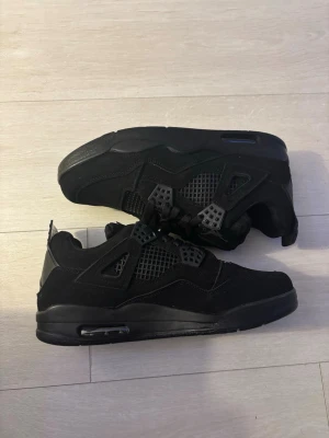 Jordan 4 Black cat - Säljer ett par helsvarta sneakers med meshdetaljer på sidorna och plastdetaljer vid snörningen. Skorna har en chunky sula med synlig luftbubbla och är tillverkade i mockaliknande material. Perfekta för dig som gillar en clean och sportig look.                       OBS: kvitto, samt box finns ej.