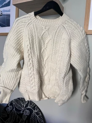 Vit kabelstickad tröja Polo Ralph Lauren - Kabelstickad vit tröja från Polo Ralph Lauren i storlek S. Tröjan har rund halsringning, ribbade muddar och ett klassiskt flätmönster framtill. Perfekt för dig som gillar en tidlös och mysig look.