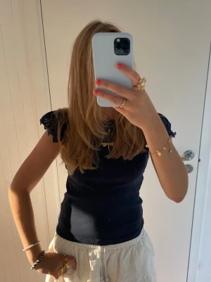 Mörkblå topp med spetsärmar - Snygg mörkblå topp med ribbad struktur och korta spetsärmar. Toppen har en figurnära passform och är perfekt att matcha med både kjol och jeans. Materialet känns mjukt och stretchigt.