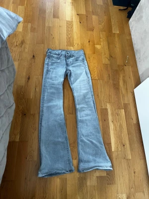 Grå bootcut jeans - Säljer ett par grå  bootcut jeans med klassisk femficksdesign och låg  midja. Jeansen har en snygg tvättad look och är tillverkade i ett stretchigt denimtyg som sitter bekvämt. Perfekta för dig som gillar en retroinspirerad stil.