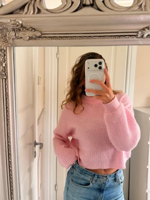 Ljusrosa cropped stickad tröja - Säljer en ljusrosa stickad tröja med croppad passform och ribbade muddar. Tröjan har en högre rund halsringning och är gjord i ett mjukt, fluffigt material. Perfekt för dig som gillar en avslappnad men trendig stil. Tröjan är använd och tvättad så den är något nopprig 