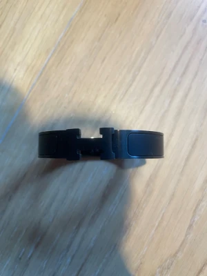 Svart armband från H med påse  - Snyggt svart armband från H i metall med klassisk H-detalj framtill. Armbandet har en stilren och modern design som passar perfekt till din outfit. Levereras med original orange H-påse.